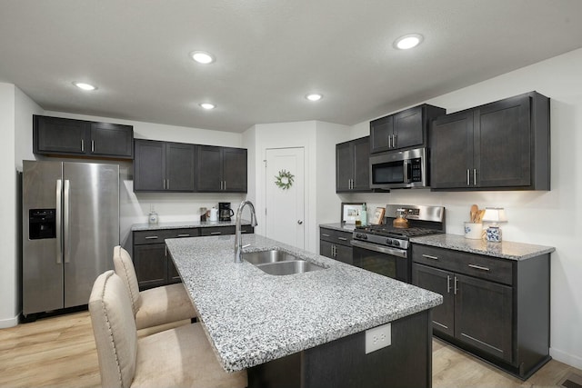 kitchen with appliances with stainless steel finishes, a kitchen breakfast bar, sink, light hardwood / wood-style flooring, and an island with sink