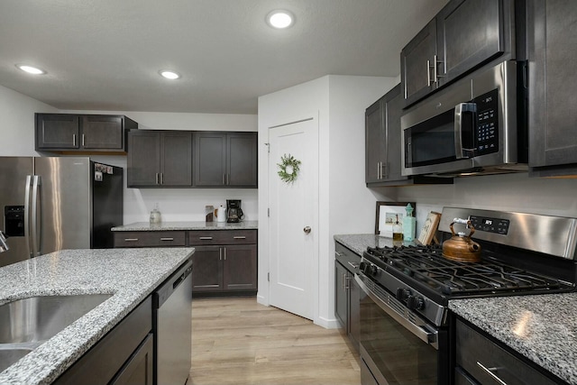 kitchen featuring light stone counters, dark brown cabinets, stainless steel appliances, sink, and light hardwood / wood-style flooring