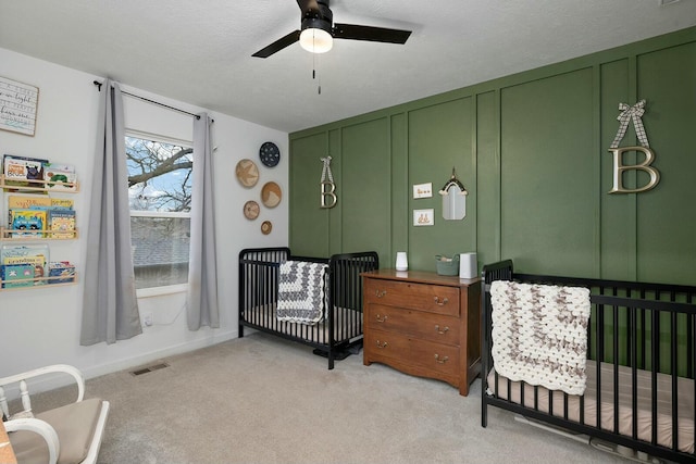 carpeted bedroom with ceiling fan, a crib, and a textured ceiling