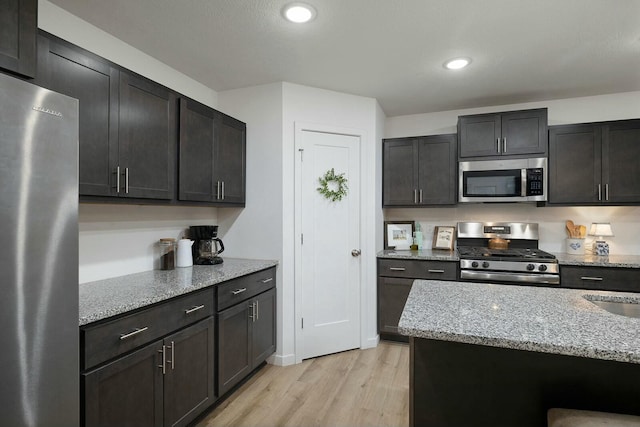 kitchen with a kitchen island, light stone countertops, light wood-type flooring, and stainless steel appliances