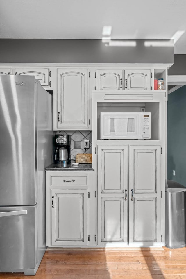 kitchen with tasteful backsplash, stainless steel refrigerator, white cabinetry, and light wood-type flooring