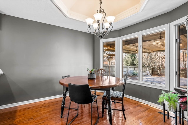 dining space with hardwood / wood-style floors, a tray ceiling, and a notable chandelier