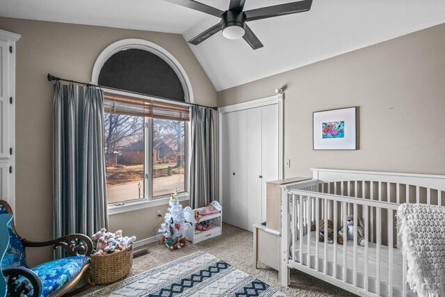 bedroom with vaulted ceiling, ceiling fan, light colored carpet, a crib, and a closet