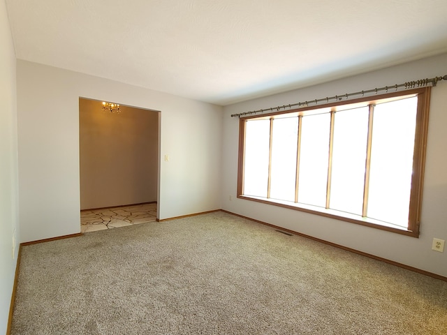 spare room featuring light colored carpet, a notable chandelier, and a wealth of natural light