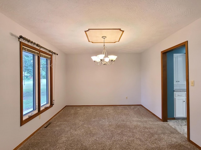 carpeted spare room featuring an inviting chandelier and a textured ceiling