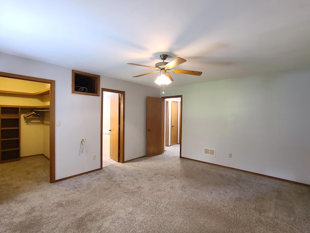 unfurnished bedroom with a walk in closet, light colored carpet, ceiling fan, and a closet