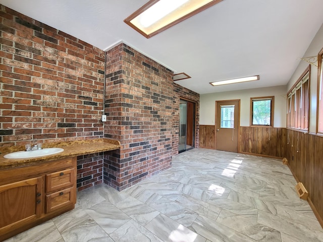 interior space with brick wall, built in desk, wooden walls, sink, and light stone countertops