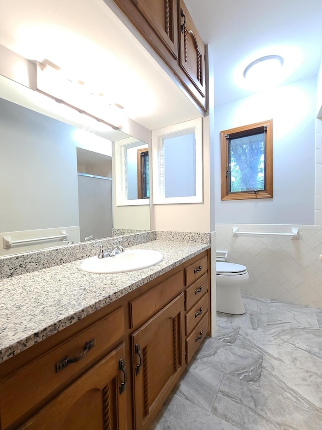 bathroom featuring vanity, toilet, tile walls, and a shower