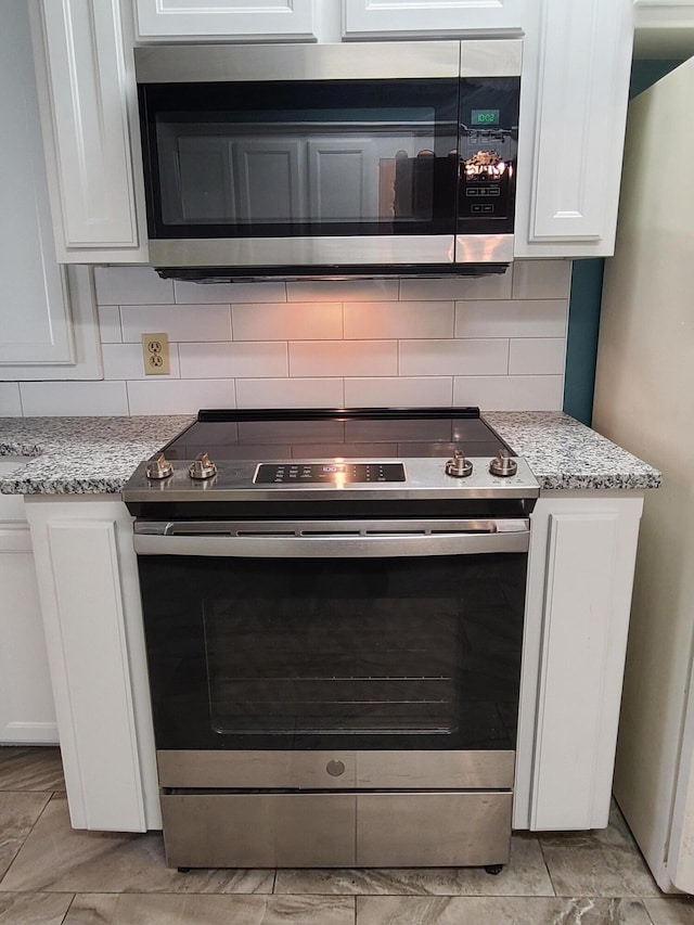 kitchen with tasteful backsplash, appliances with stainless steel finishes, light stone countertops, and white cabinets