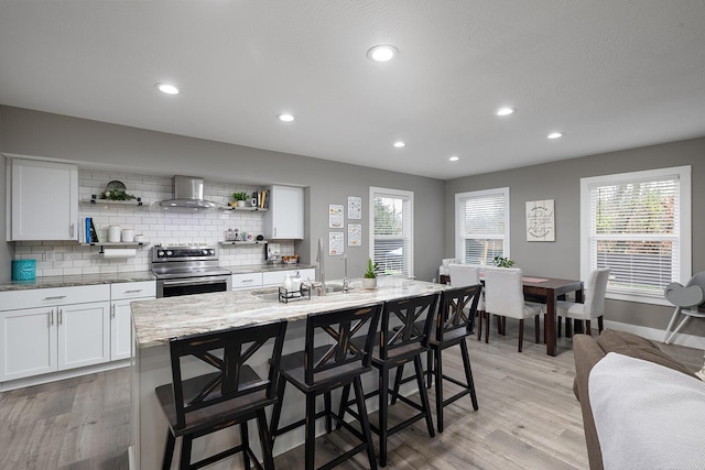 kitchen with a breakfast bar, white cabinetry, stainless steel range with electric stovetop, and an island with sink