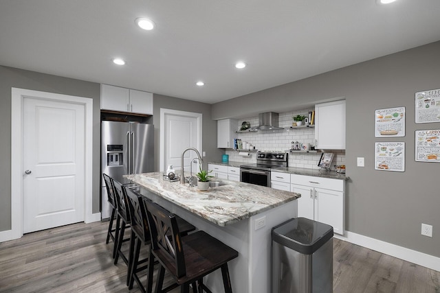 kitchen with stainless steel appliances, white cabinetry, a kitchen island with sink, and wall chimney exhaust hood