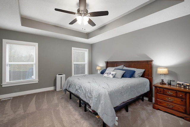 carpeted bedroom with a raised ceiling and ceiling fan