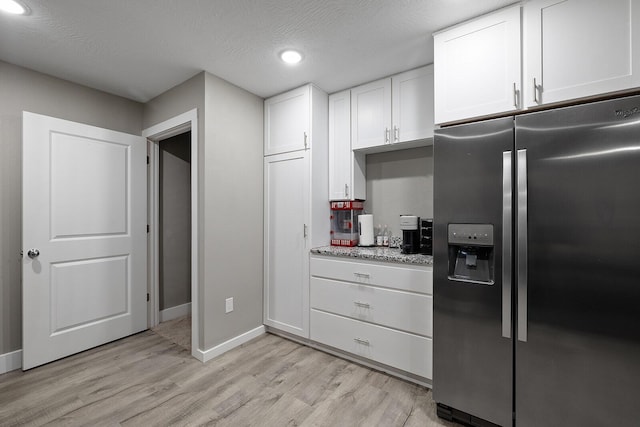 kitchen featuring stainless steel refrigerator with ice dispenser, light stone counters, a textured ceiling, white cabinets, and light hardwood / wood-style floors