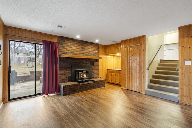 unfurnished living room featuring wood-type flooring, a textured ceiling, a wood stove, and wooden walls