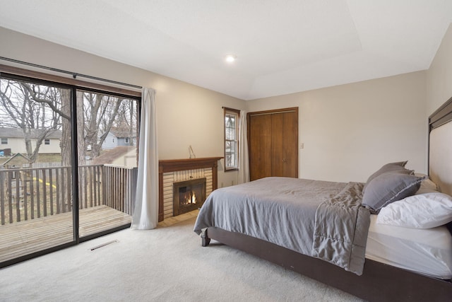 carpeted bedroom featuring access to outside, a raised ceiling, and a fireplace