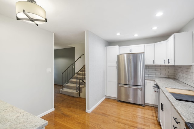 kitchen featuring backsplash, white cabinets, light stone countertops, appliances with stainless steel finishes, and light hardwood / wood-style floors