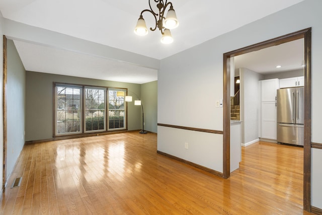 empty room with a chandelier and light wood-type flooring