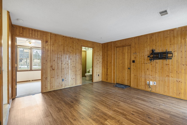 spare room with wood walls, wood-type flooring, and a textured ceiling