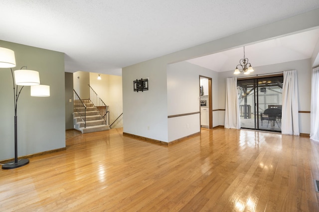 spare room with a textured ceiling, light wood-type flooring, vaulted ceiling, and a notable chandelier