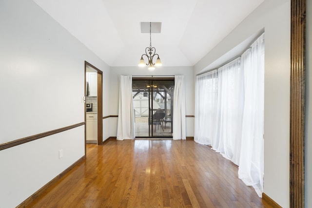 spare room with wood-type flooring, vaulted ceiling, and an inviting chandelier