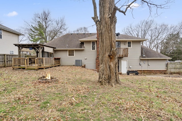 back of property with a fire pit, a lawn, a wooden deck, and central AC