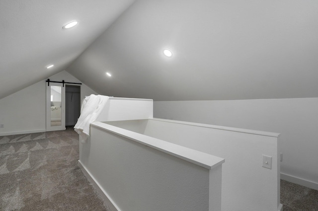 additional living space with dark colored carpet, a barn door, and lofted ceiling