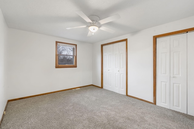 unfurnished bedroom featuring multiple closets, ceiling fan, and carpet