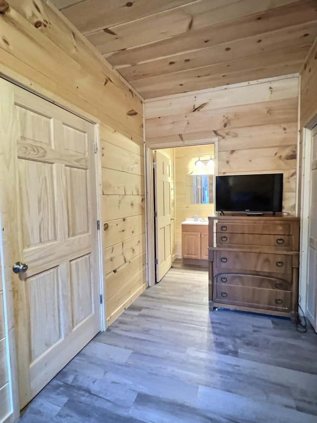 interior space with light wood-type flooring, connected bathroom, wood ceiling, and wood walls