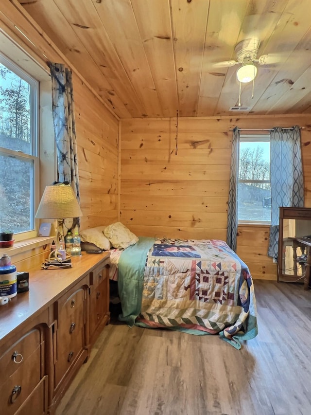 bedroom with wooden walls, light hardwood / wood-style flooring, multiple windows, and wooden ceiling