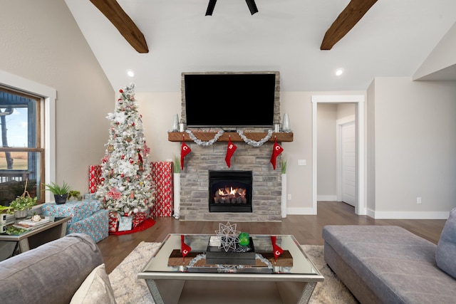 living room featuring hardwood / wood-style flooring, vaulted ceiling with beams, ceiling fan, and a stone fireplace