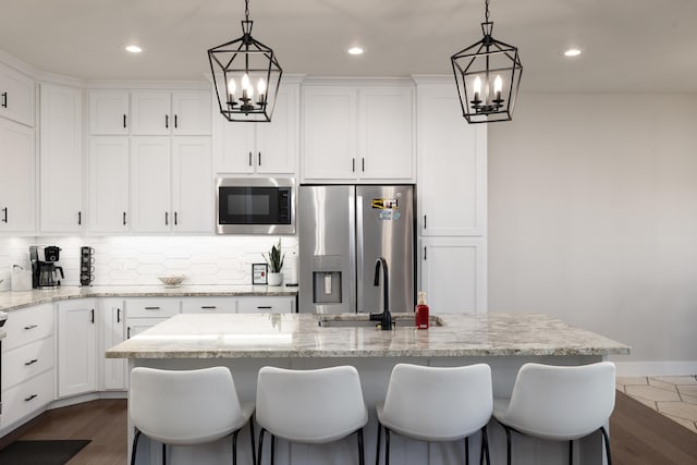 kitchen with a center island with sink, white cabinets, appliances with stainless steel finishes, tasteful backsplash, and light stone counters