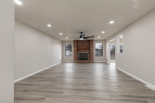 unfurnished living room with hardwood / wood-style floors, ceiling fan, a textured ceiling, and a brick fireplace