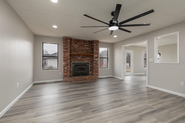 unfurnished living room with a wood stove, ceiling fan, hardwood / wood-style floors, and a healthy amount of sunlight