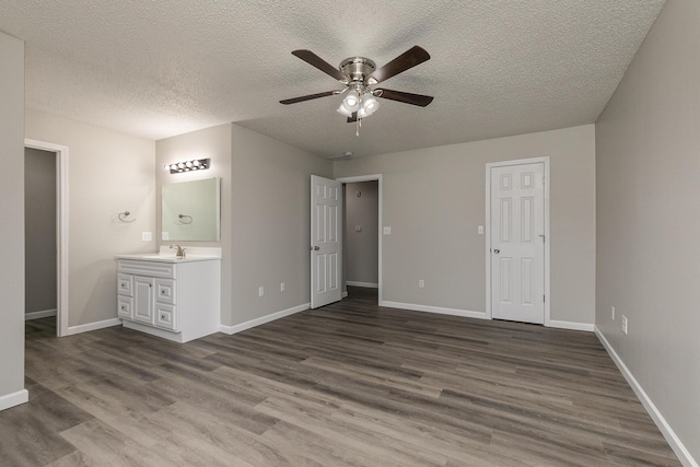 unfurnished bedroom with dark wood-type flooring, ensuite bathroom, sink, ceiling fan, and a textured ceiling