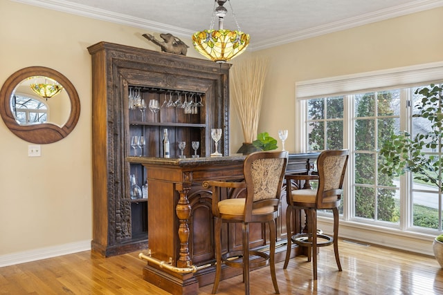 bar with pendant lighting, light hardwood / wood-style floors, crown molding, and a healthy amount of sunlight