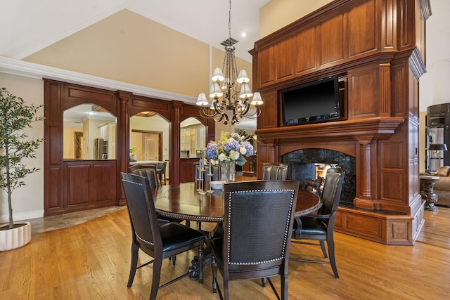 dining space featuring a premium fireplace, light hardwood / wood-style flooring, a towering ceiling, a chandelier, and ornamental molding