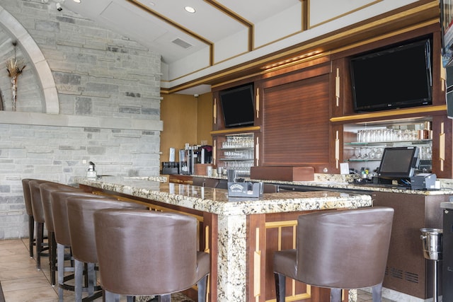 kitchen featuring a kitchen breakfast bar, kitchen peninsula, light stone countertops, and vaulted ceiling