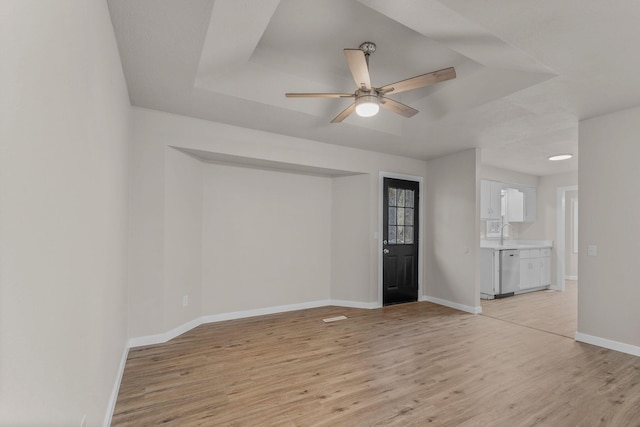 unfurnished room featuring ceiling fan, a raised ceiling, light wood-type flooring, and sink