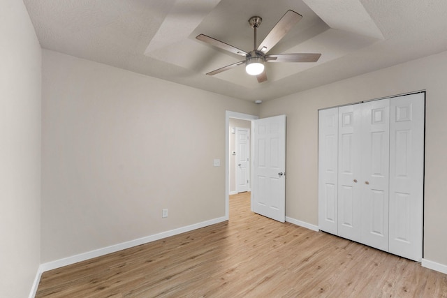 unfurnished bedroom featuring a raised ceiling, ceiling fan, a closet, and light wood-type flooring