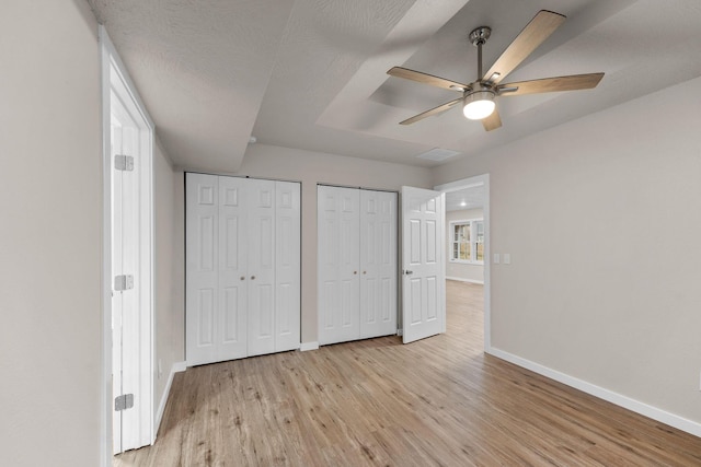 unfurnished bedroom with ceiling fan, light wood-type flooring, and multiple closets