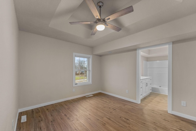 unfurnished room with ceiling fan, a tray ceiling, and light hardwood / wood-style flooring