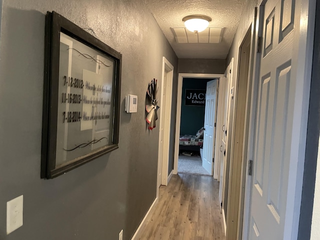 corridor with a textured ceiling and light hardwood / wood-style flooring