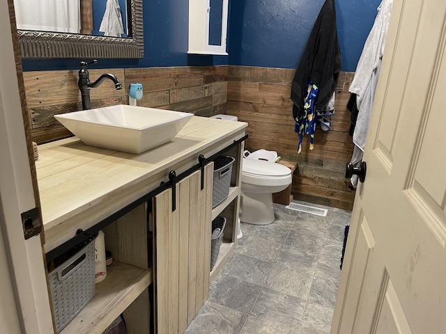 bathroom with vanity, wooden walls, and toilet