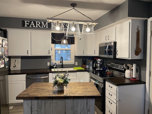 kitchen featuring decorative light fixtures, a kitchen island, wooden counters, and appliances with stainless steel finishes