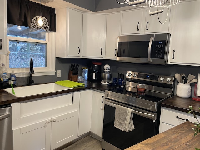 kitchen with stainless steel appliances, butcher block counters, sink, and white cabinets