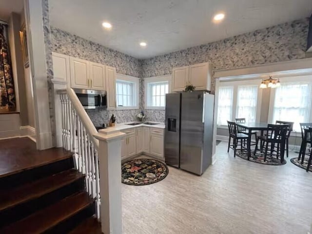 kitchen with white cabinets, sink, light wood-type flooring, stainless steel appliances, and a chandelier