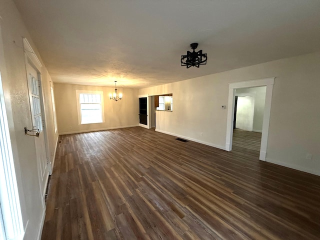 unfurnished living room featuring dark wood-type flooring and an inviting chandelier