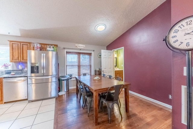 dining area featuring light wood-type flooring, a textured ceiling, and vaulted ceiling