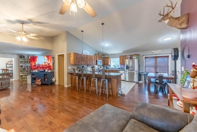 living room with ceiling fan, light wood-type flooring, a textured ceiling, and vaulted ceiling