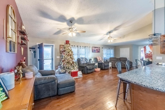 living room with lofted ceiling, ceiling fan, wood-type flooring, and a textured ceiling